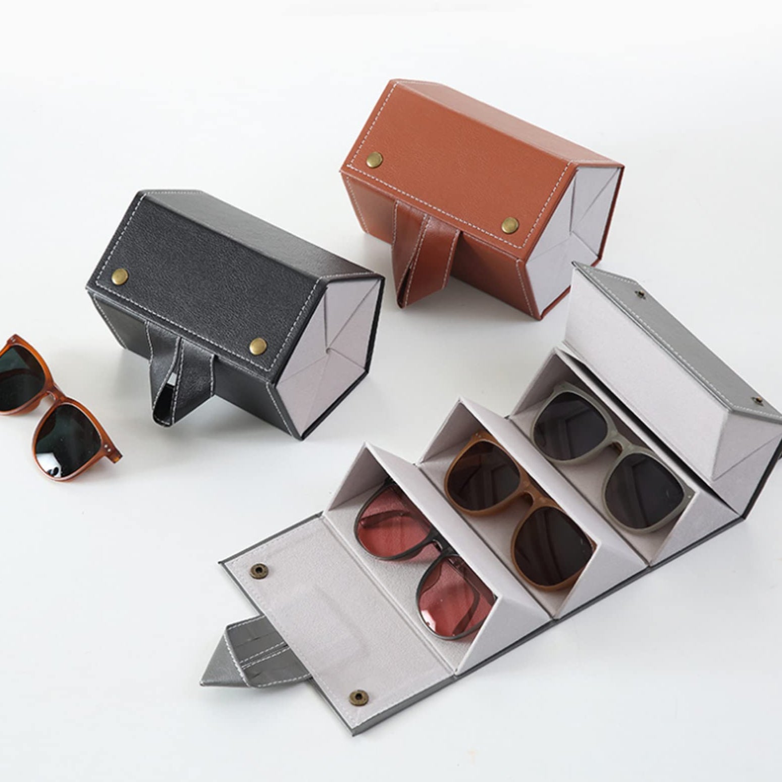 Three sunglasses cases in different colors with sunglasses inside on a white background